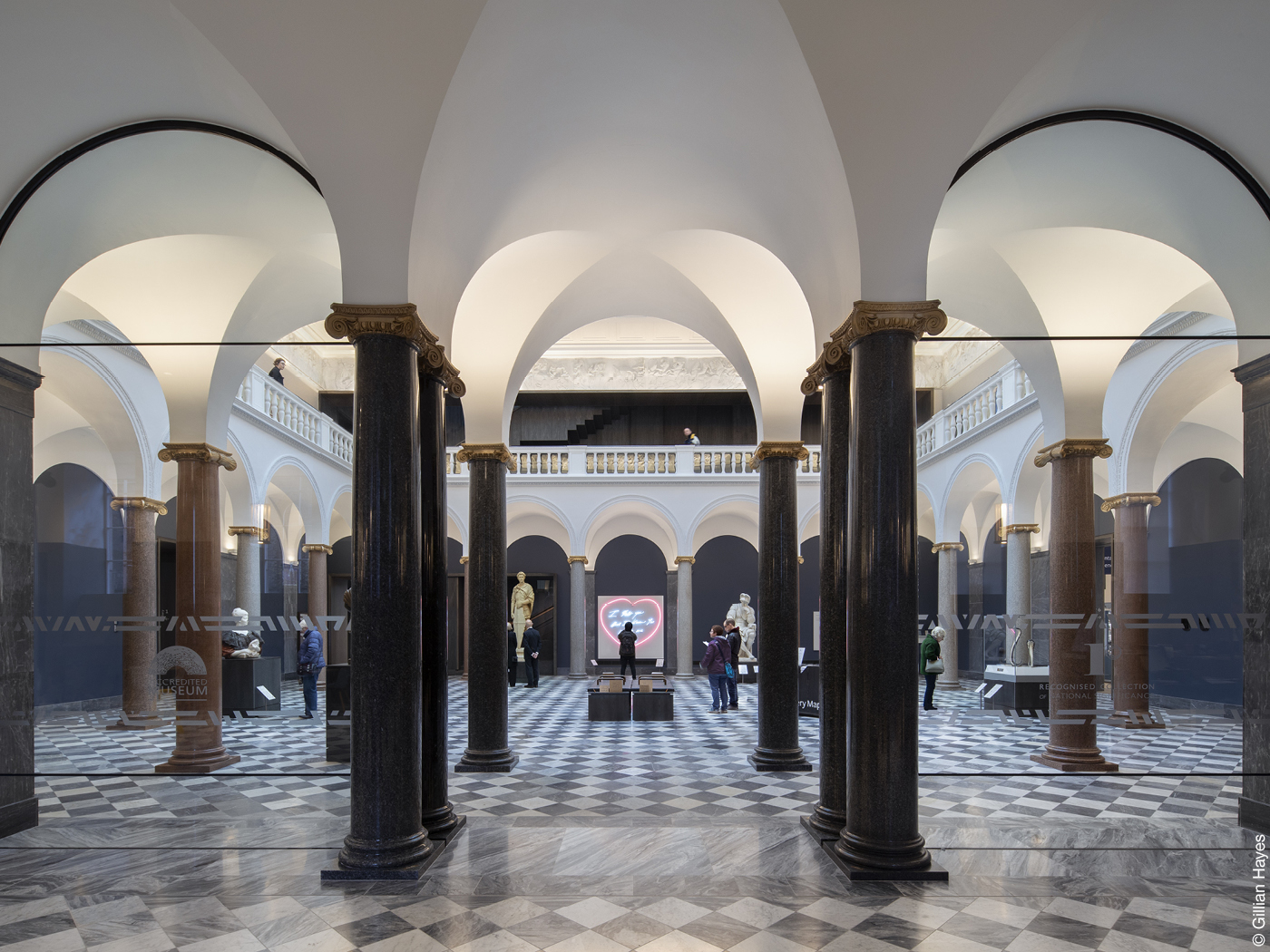 Helle Halle mit dunklen Säulen und gekacheltem Boden.