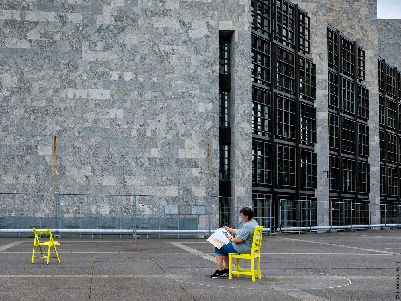 Frau sitzt auf einem gelben Stuhl vor der steinernen Fassade des Arne Jacobsen Rathauses in Mainz.