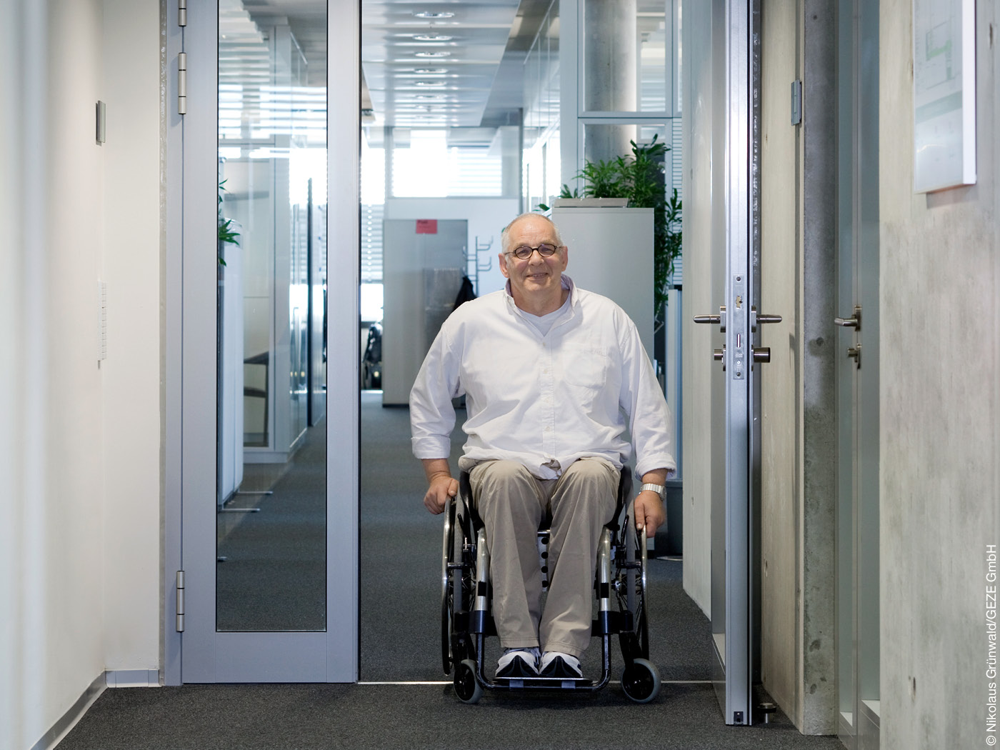 Mann im Rollstuhl fährt auf einem Flur durch eine Tür.