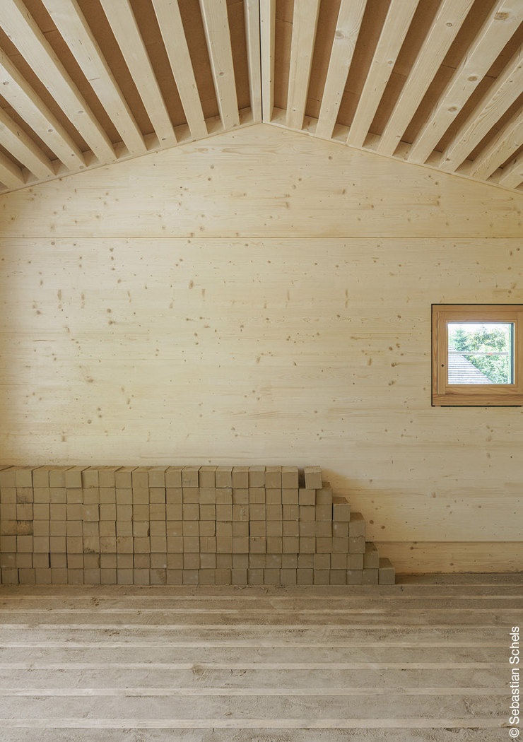 Gestapelte Lehmziegel vor einer Holzwand