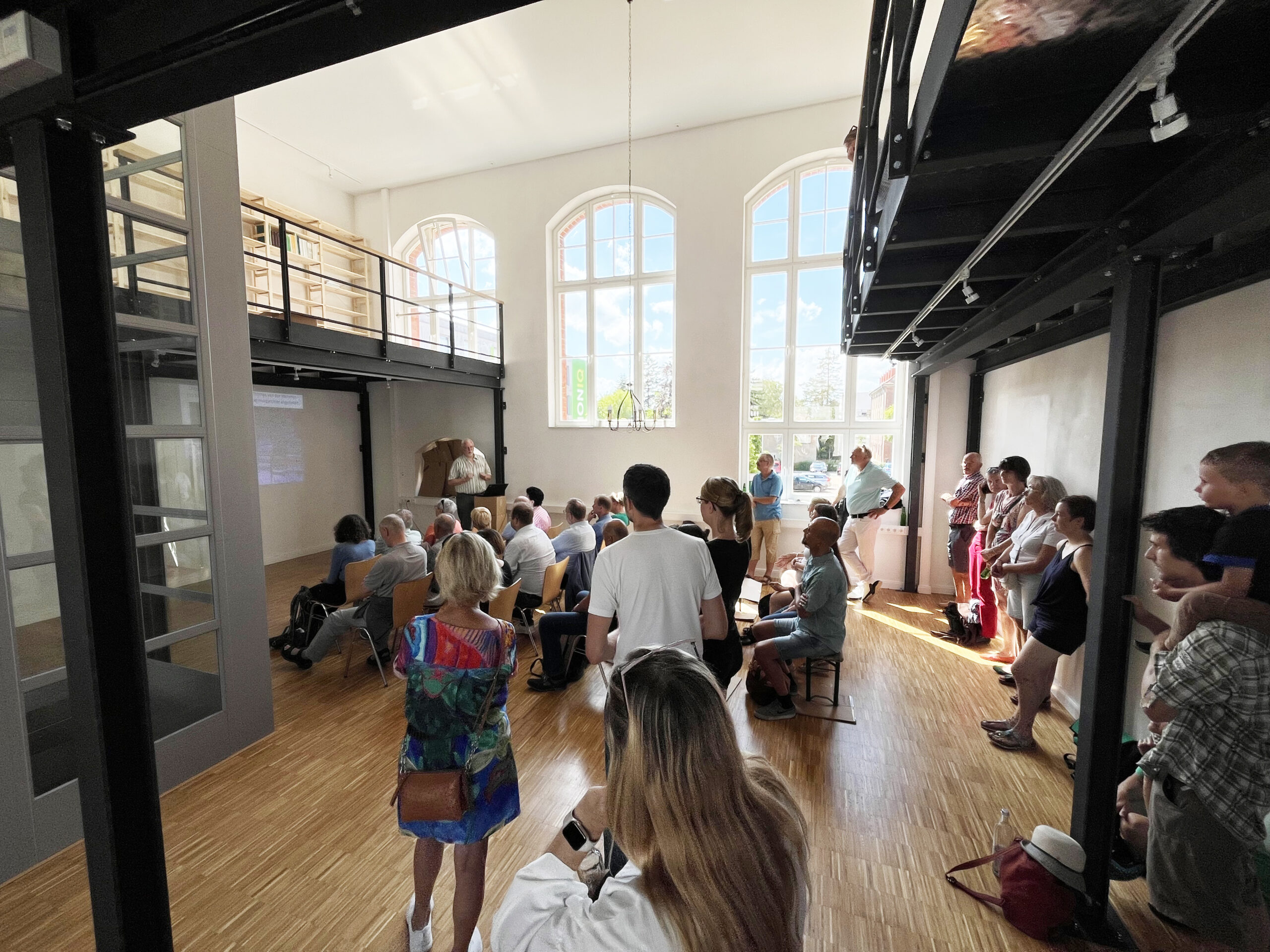 Heller Raum mit hohen Fenstern und vielen Menschen im Raum