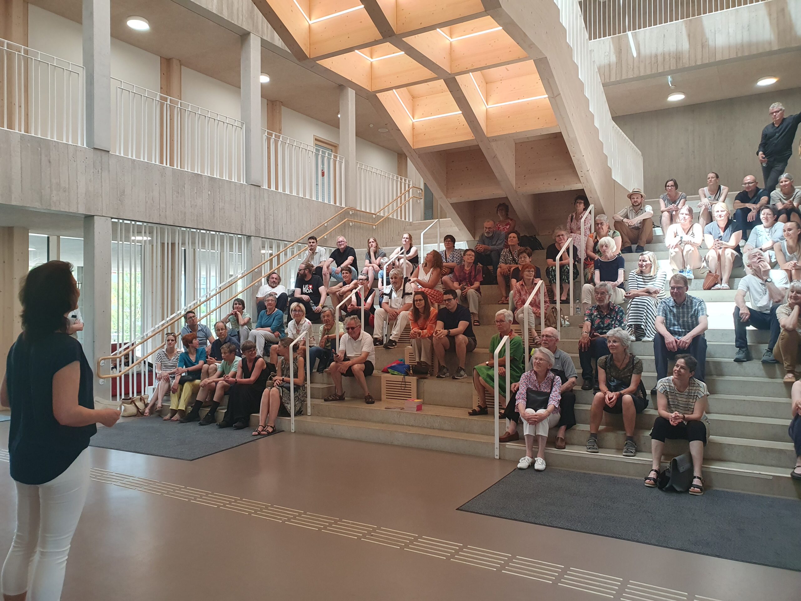 Männer und Frauen sitzen im Treppenhaus eines Schulgebäudes auf den Stufen.
