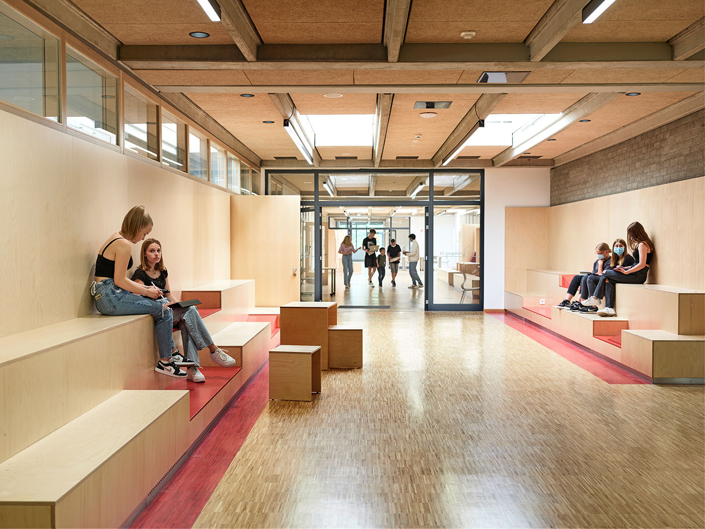 Indoor-Pausenhof in der Kooperativen Gesamtschule in Leeste mit Sitzstufen aus Holz, auf denen Kinder sitzen.