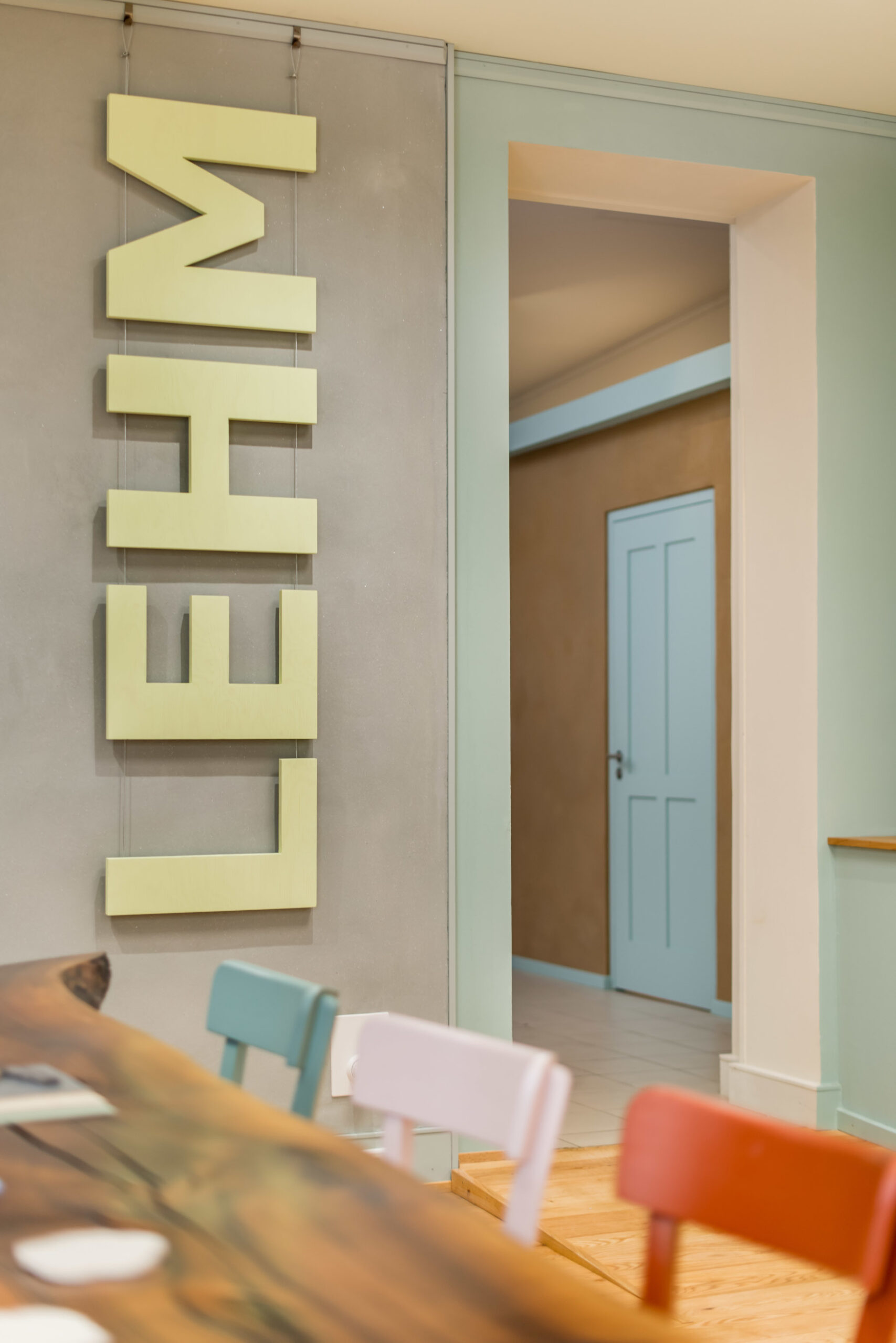 Laden mit Tisch, farbigen Stühlen und Wänden und Schriftzug "Lehm"