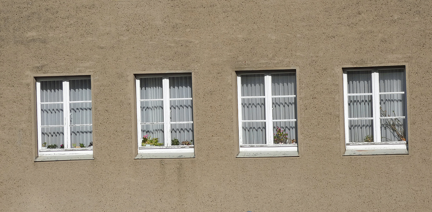 Vier Fenster in einer glatten, graubraunen Fassade