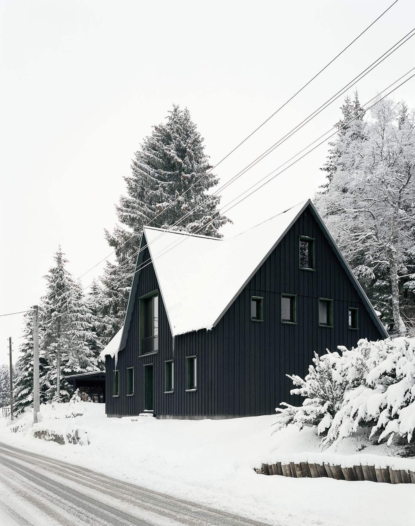 Schwarzes Holzhaus im Erzgebirge zwischen verschneiten Tannen