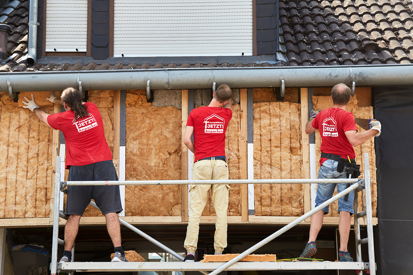 Drei Menschen dämmen die Fassade eines Hauses