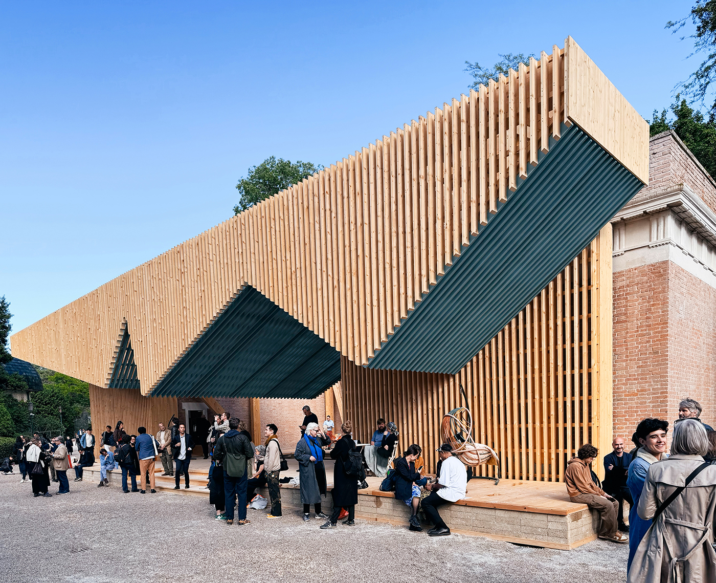 Gezacktes Vordach aus hellem Holz eines Pavillons mit Menschen davor