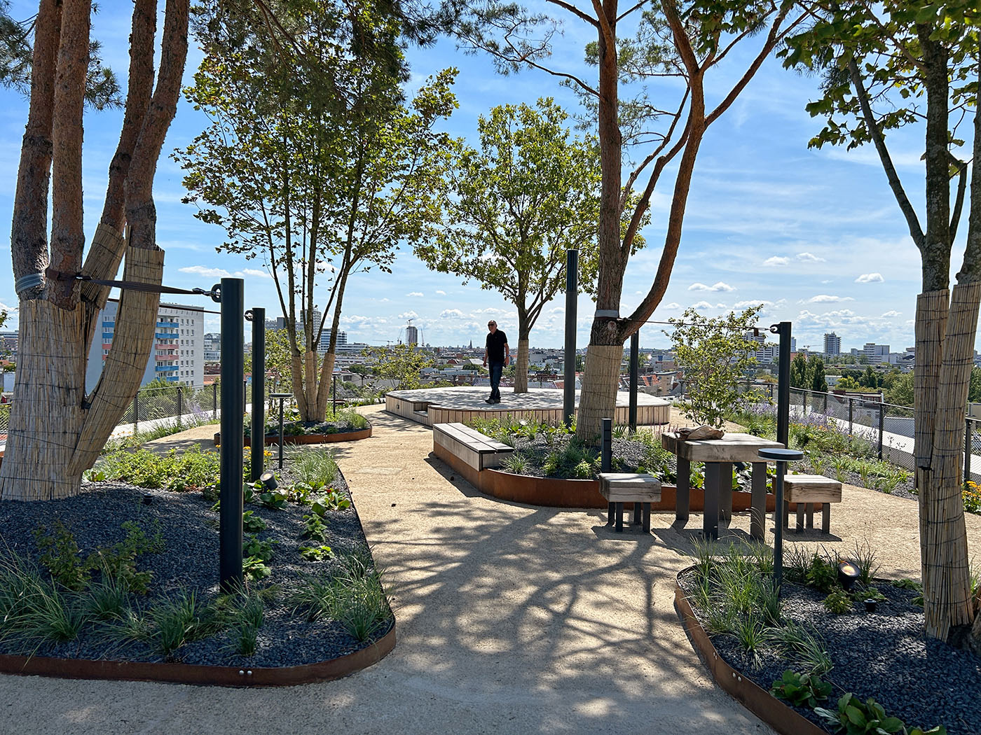 Dachterrasse mit Bäumen, Büschen und Pflanzen, einem Tisch und Stühlen und einem Holzdeck