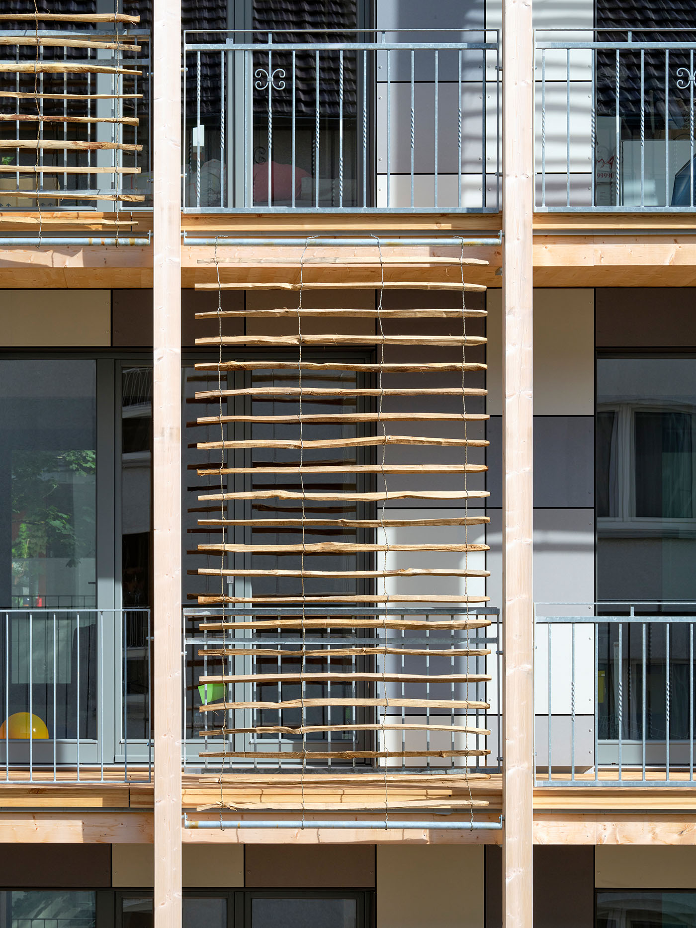 Balkone mit bodentiefen Fenstern und überdimensionalen Rollos mit Holzlamellen.