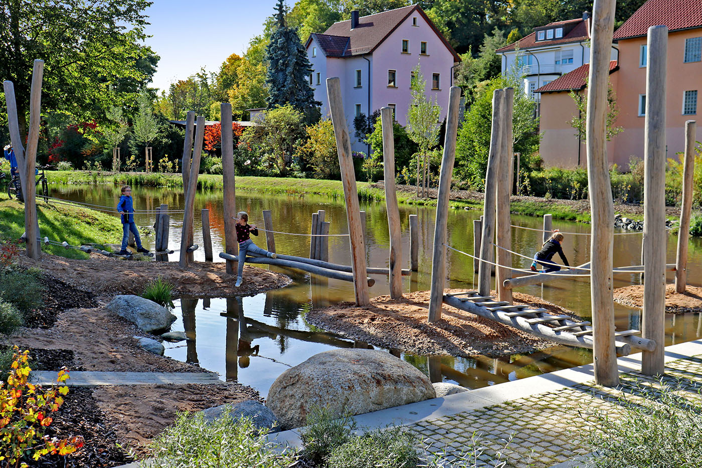 Wasserspielplatz an einem Fluss mit Wohnhäusern an den Ufern