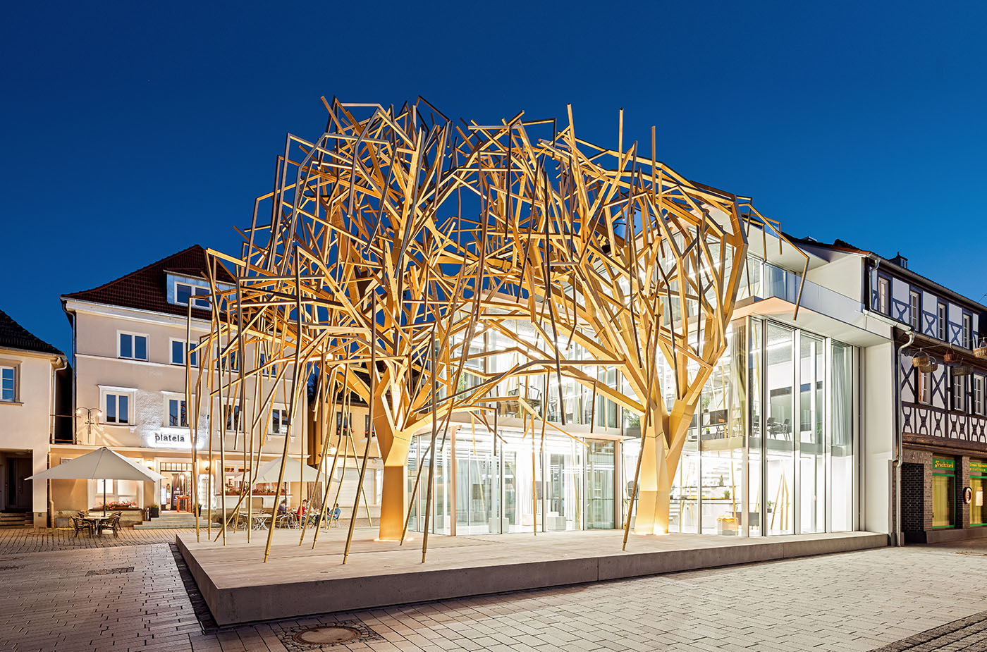 Ein von goldenen Stahlweiden überwölbter Pavillon auf einem Marktplatz.