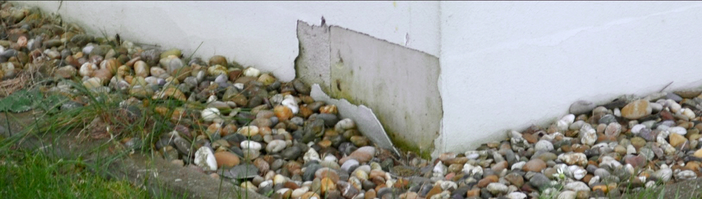 Hauswand mit abgeplatztem Putz und Kies davor