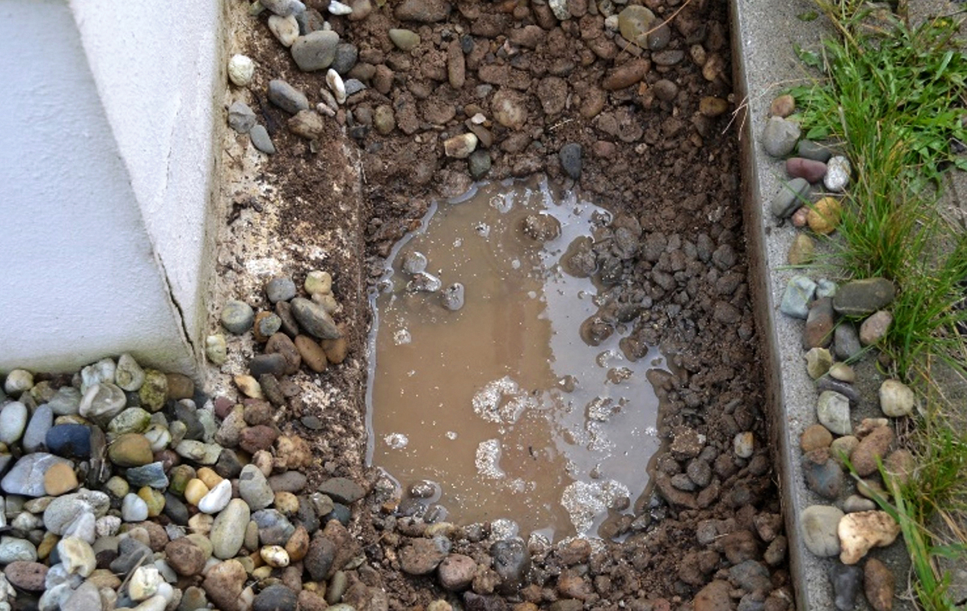 Stehendes Wasser in Kiesstreifen an hauswand