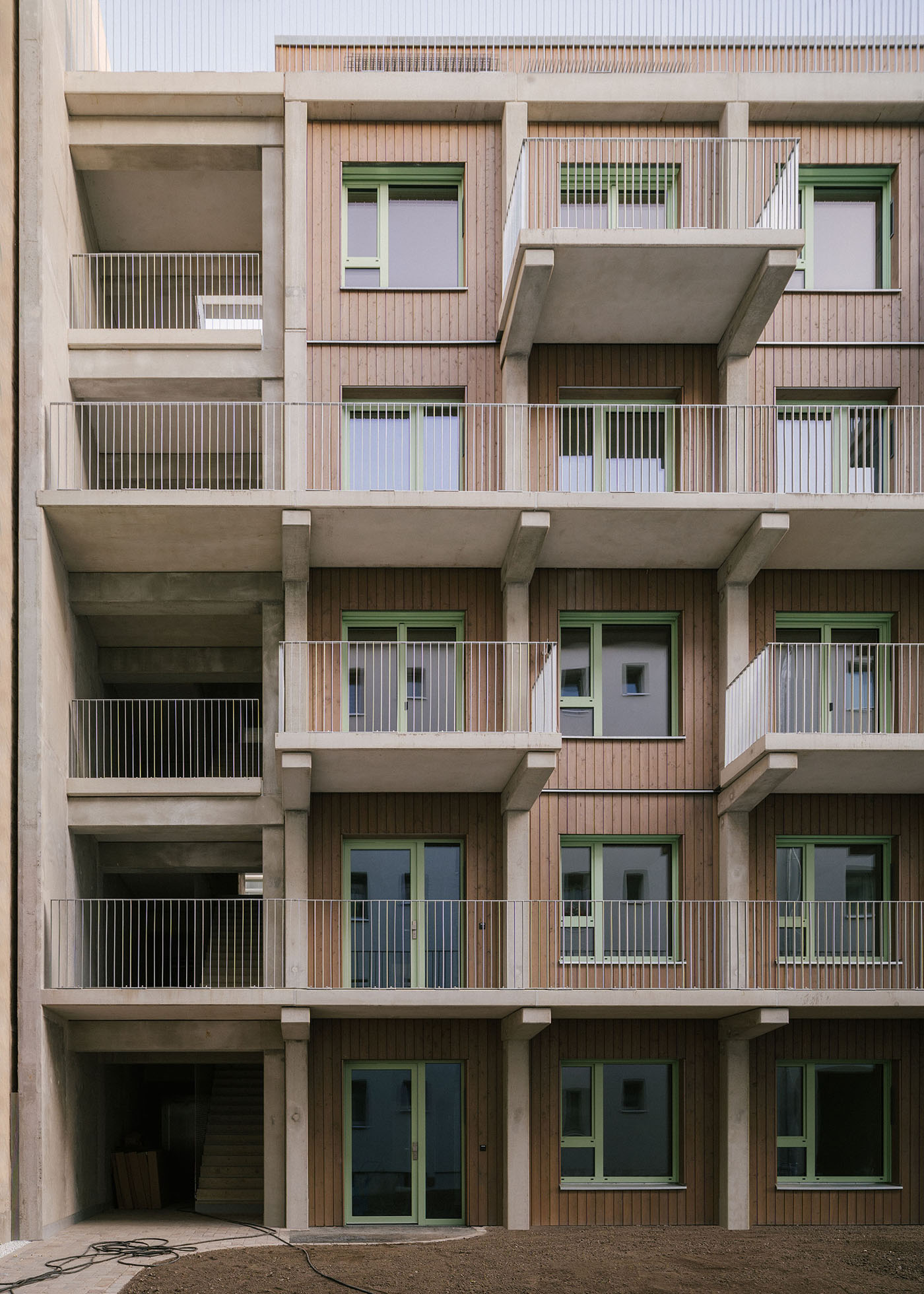 Haus in Modulbauweise mit Holzfassade, grünen Fenstern und Balkonen aus Beton.