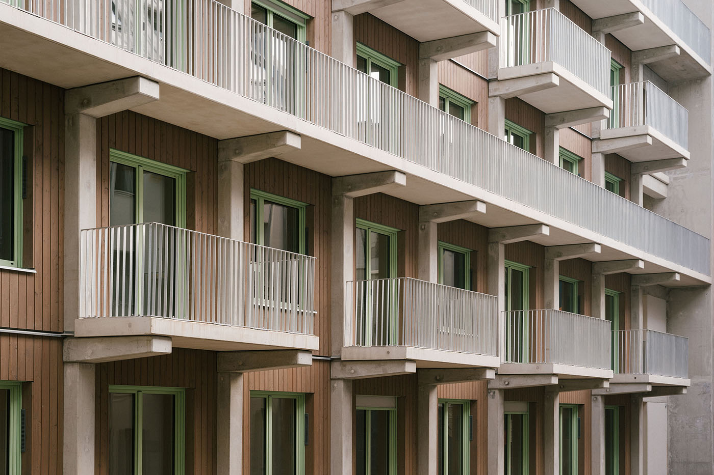 Wohngebäude mit Holzfassade, quadratischen Fenstern mit grünen Fensterrahmen und weißen Balkons