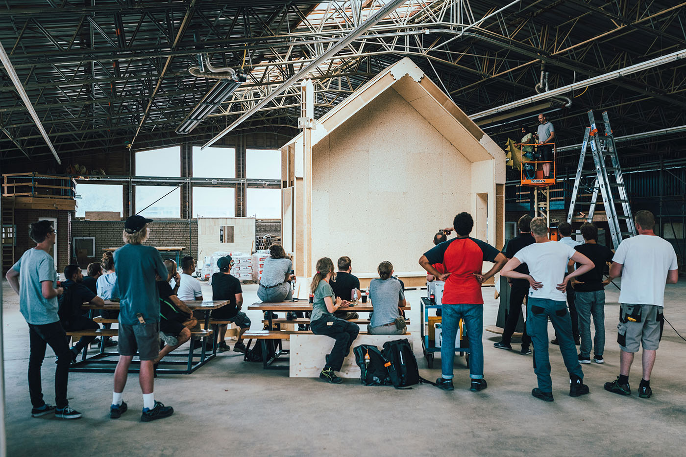 Junge Menschen stehen in einer Halle vor einem Modellhaus